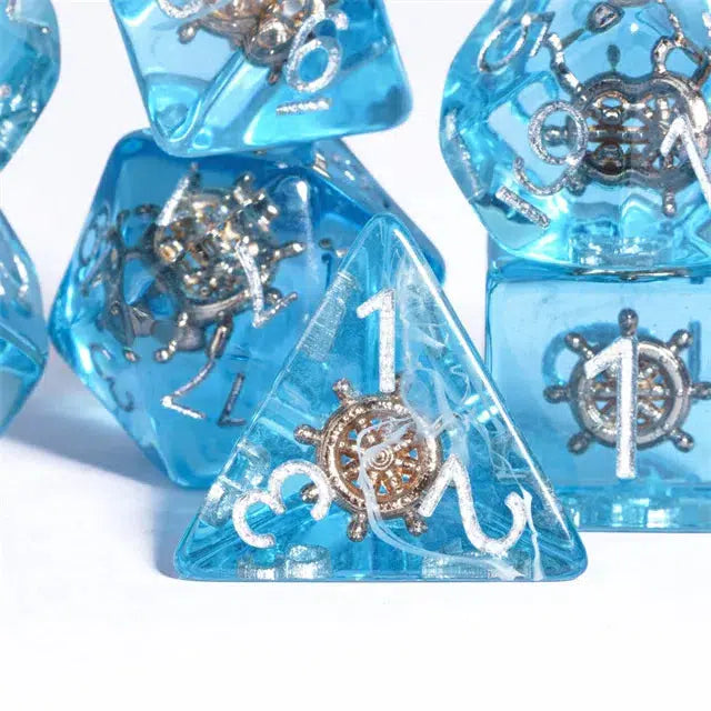 A stunning set of translucent blue polyhedral dice, perfect for role-playing games like Dungeons and Dragons. Featuring silver ship wheel designs nestled inside, these dice boast white numbers, with a four-sided die prominently placed at the forefront.