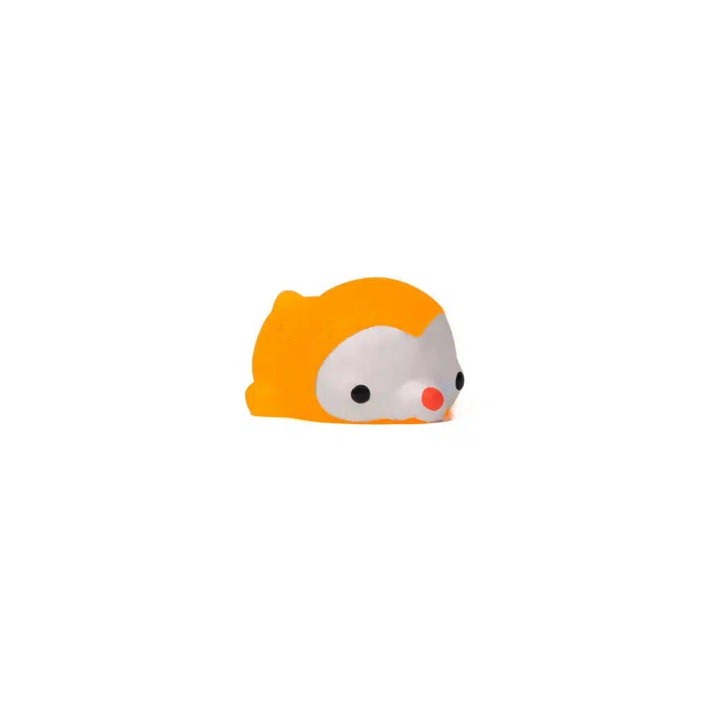 A small, orange animal squish figurine with a white face and large black eyes lies on a white background, reminiscent of toy animals often found in blind capsules.