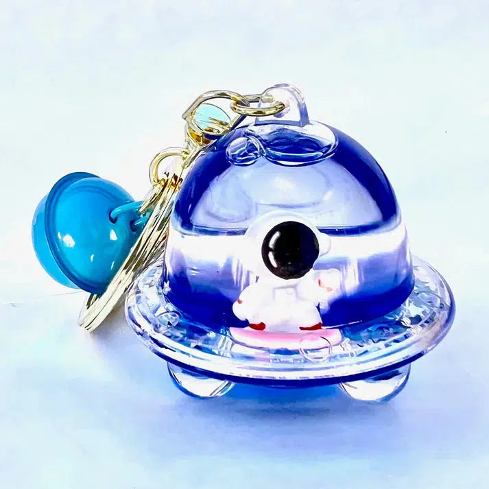 A small blue and transparent UFO-themed keychain features a tiny astronaut figure inside, attached to a larger blue disc charm, offering an out-of-this-world accessory for your collection.