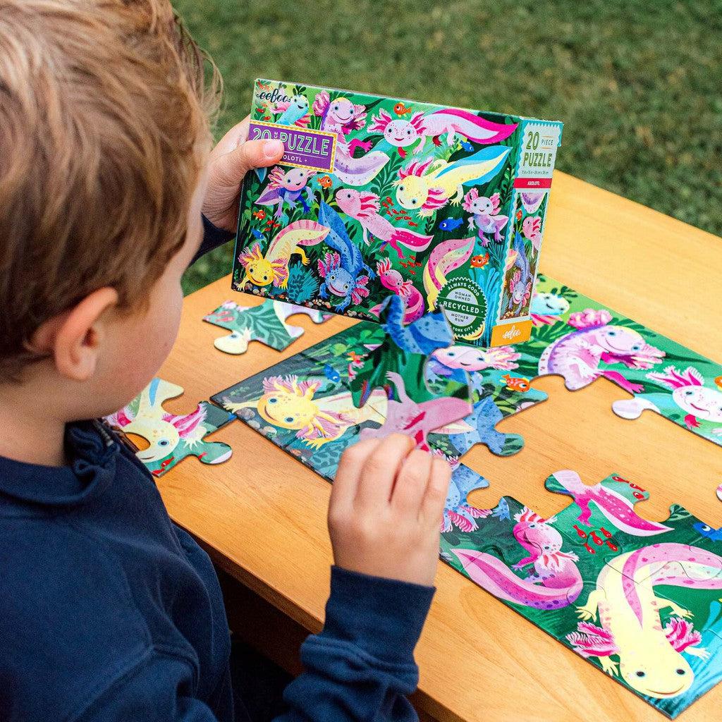 A child hones their fine motor skills as they assemble a colorful puzzle featuring axolotls on a wooden table, with the jumbo-sized puzzle pieces and box nearby.