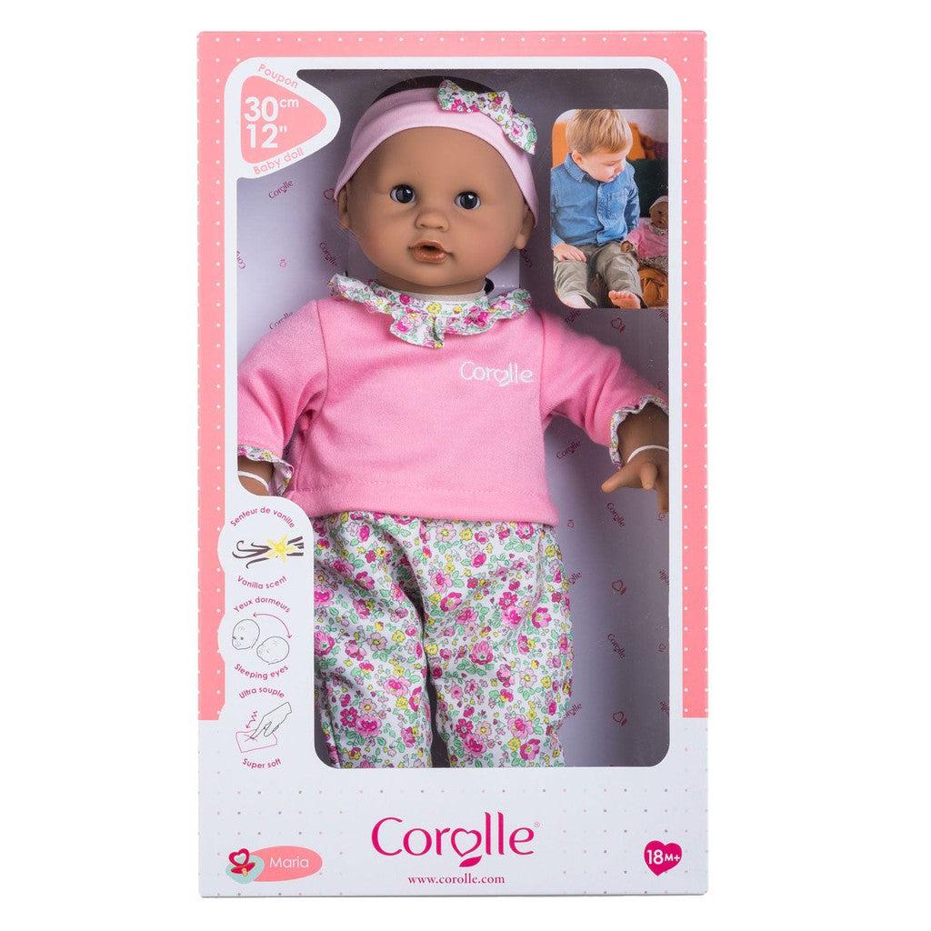 Corolle doll in a pink floral outfit inside its packaging, featuring a photo of a child playing with the doll.