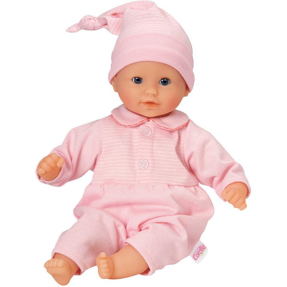 A Corolle Bébé Calin baby doll is sitting upright, showcasing its adorable pink outfit and hat.