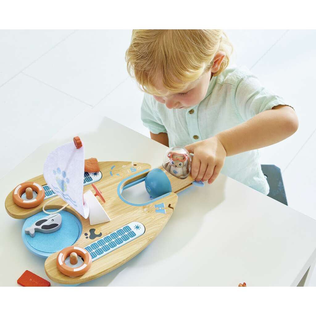 A child is playing with a wooden toy sailboat on a white table, dreaming of being an eco-conscious sailor like Ben the Otter.