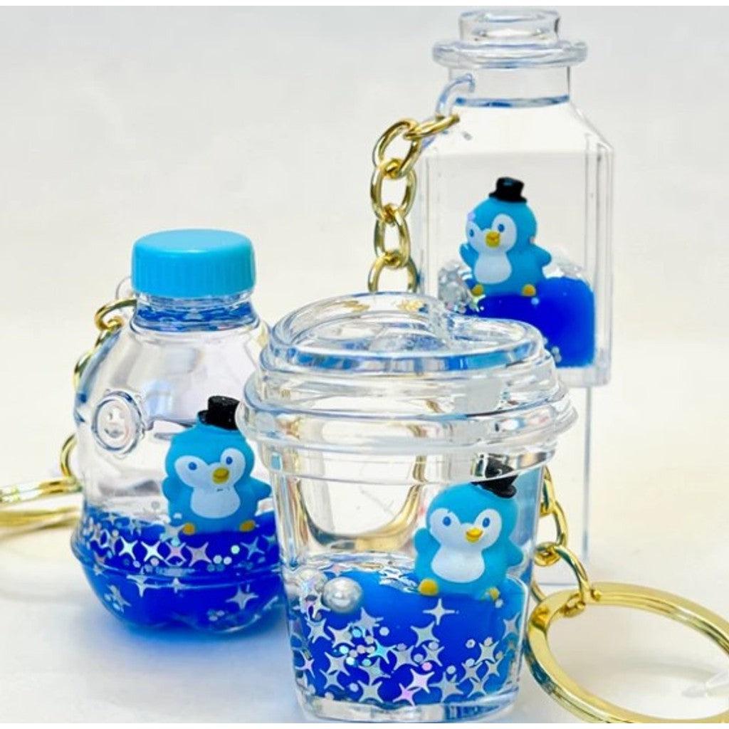 Three keychains with small penguin figurines inside clear containers of various shapes, each filled with blue liquid, bring a playful touch reminiscent of treasures found in a whimsical candy store.