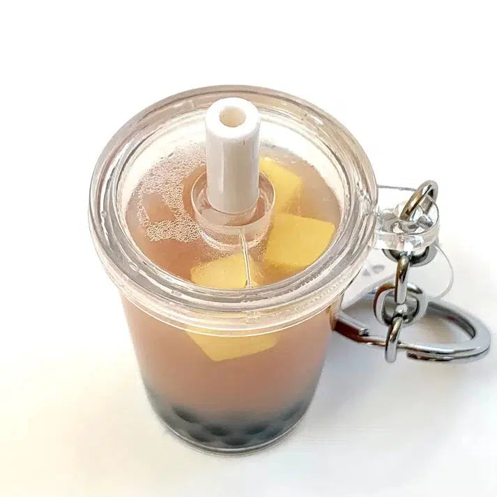 This whimsical key ring features a clear cup keychain with a straw, showcasing a delightful boba tea charm. Inside, you'll find brown liquid, black tapioca pearls, and vibrant yellow cube pieces—perfect for fans of this beloved drink!