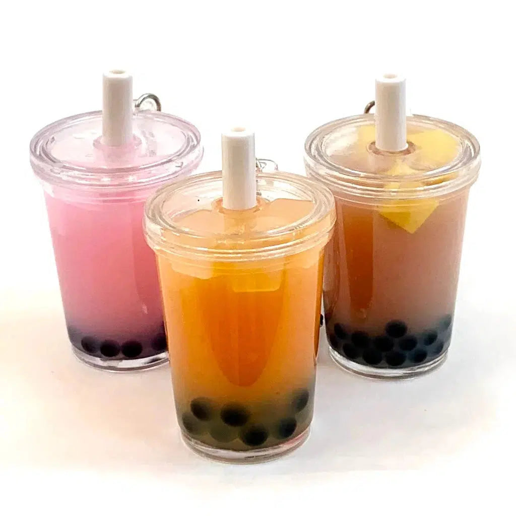 Three bubble tea drinks with straws, in pink and light orange hues, each with tapioca pearls at the bottom. These delightful beverages resemble a boba tea charm you'd find alongside toy figurines or silly animals, adding a playful touch to an already vibrant scene.