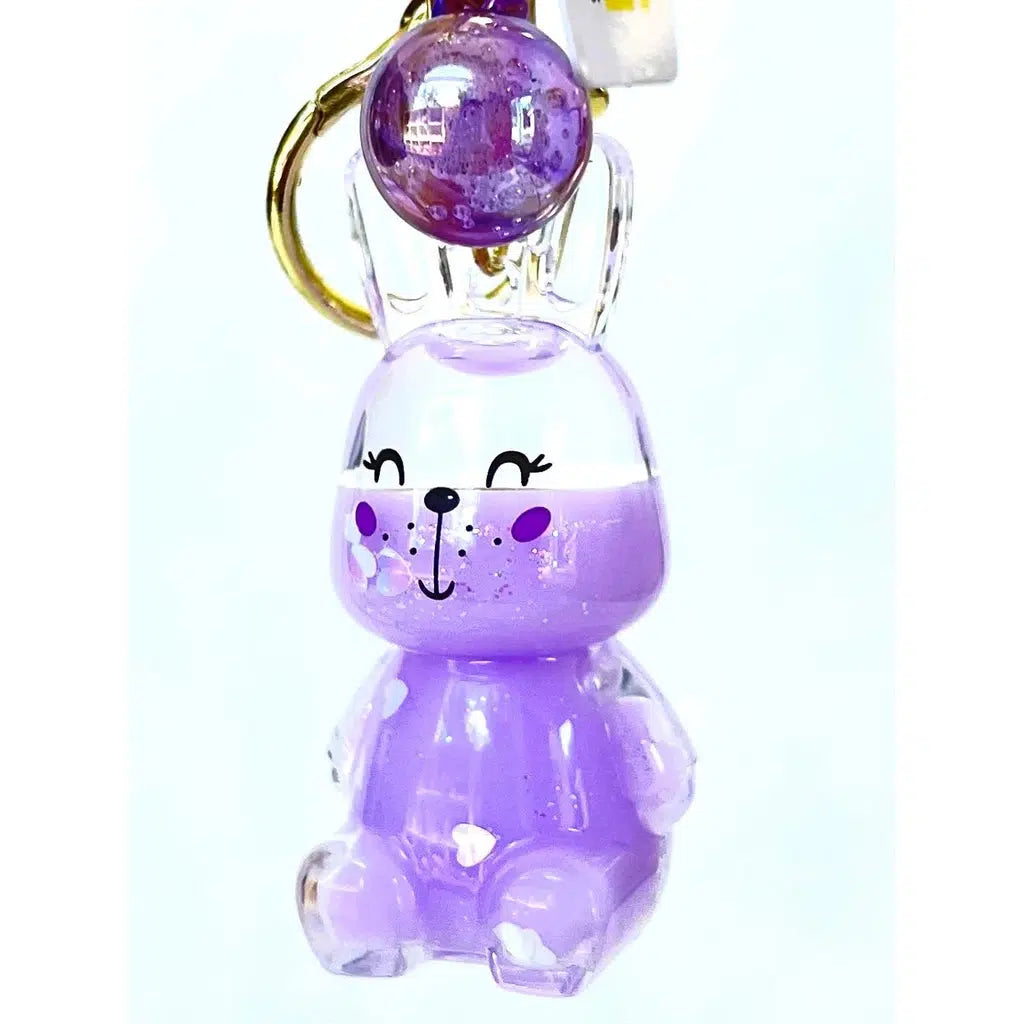 A purple bunny floaty key charm with a smiling face and closed eyes, featuring a round, glittery decoration on top. This toy figurine adds a touch of fun to your keys with its playful design.