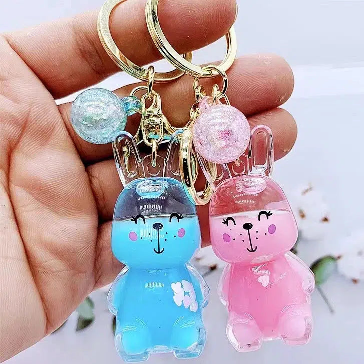 A hand holds two rabbit-shaped keychains, one blue and one pink, each with a matching glittery Bunny Floaty Key Charm.