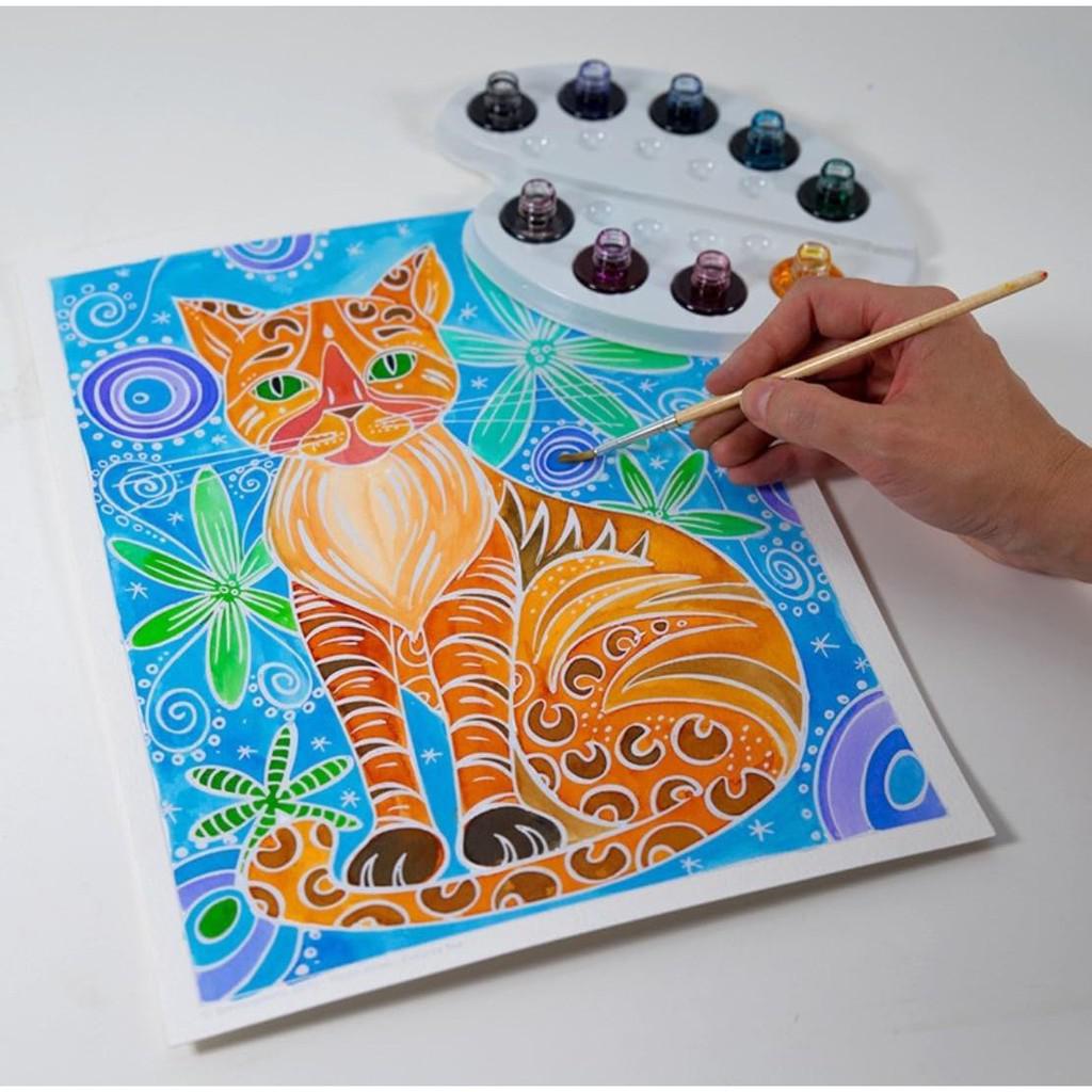 Using the Aquarellum Cats Watercolor Painting Kit from Sentosphère, a hand skillfully brings a colorful, abstract cat design to life. The background bursts with blue and green swirls and star-like shapes.