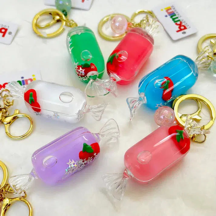 Colorful candy-shaped keychains in green, red, white, purple, and pink with gold rings and cherry motifs on a white background. These delightful Cherry Candy Floaty Key Charms come in assorted designs to add a playful touch to your keys.