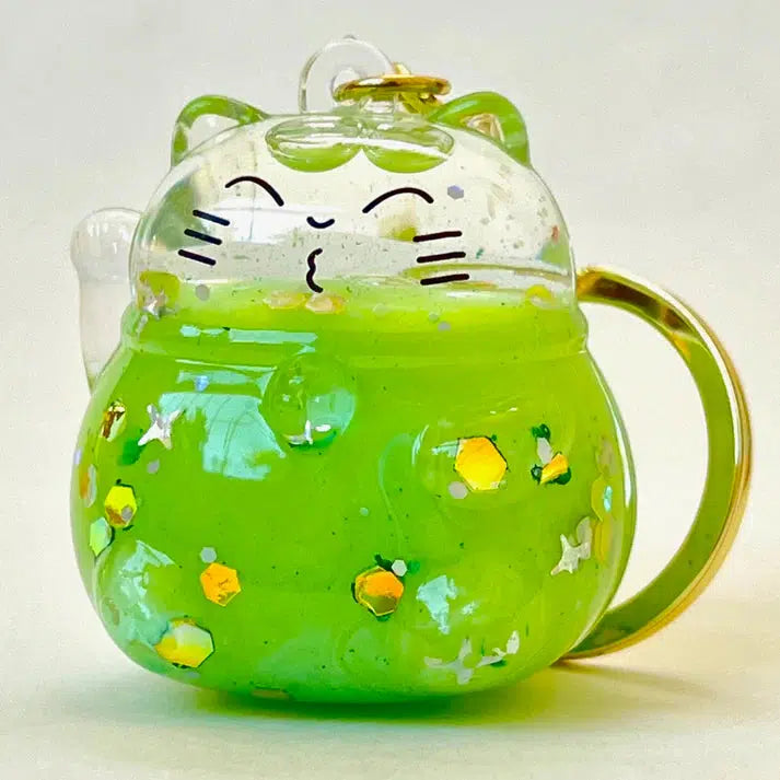 A glass ornament shaped like a lucky cat with a gold ring handle, filled with vibrant green liquid and shimmering sparkles, stands against a plain white background. This colorful cat floaty is the perfect whimsical touch to any setting.