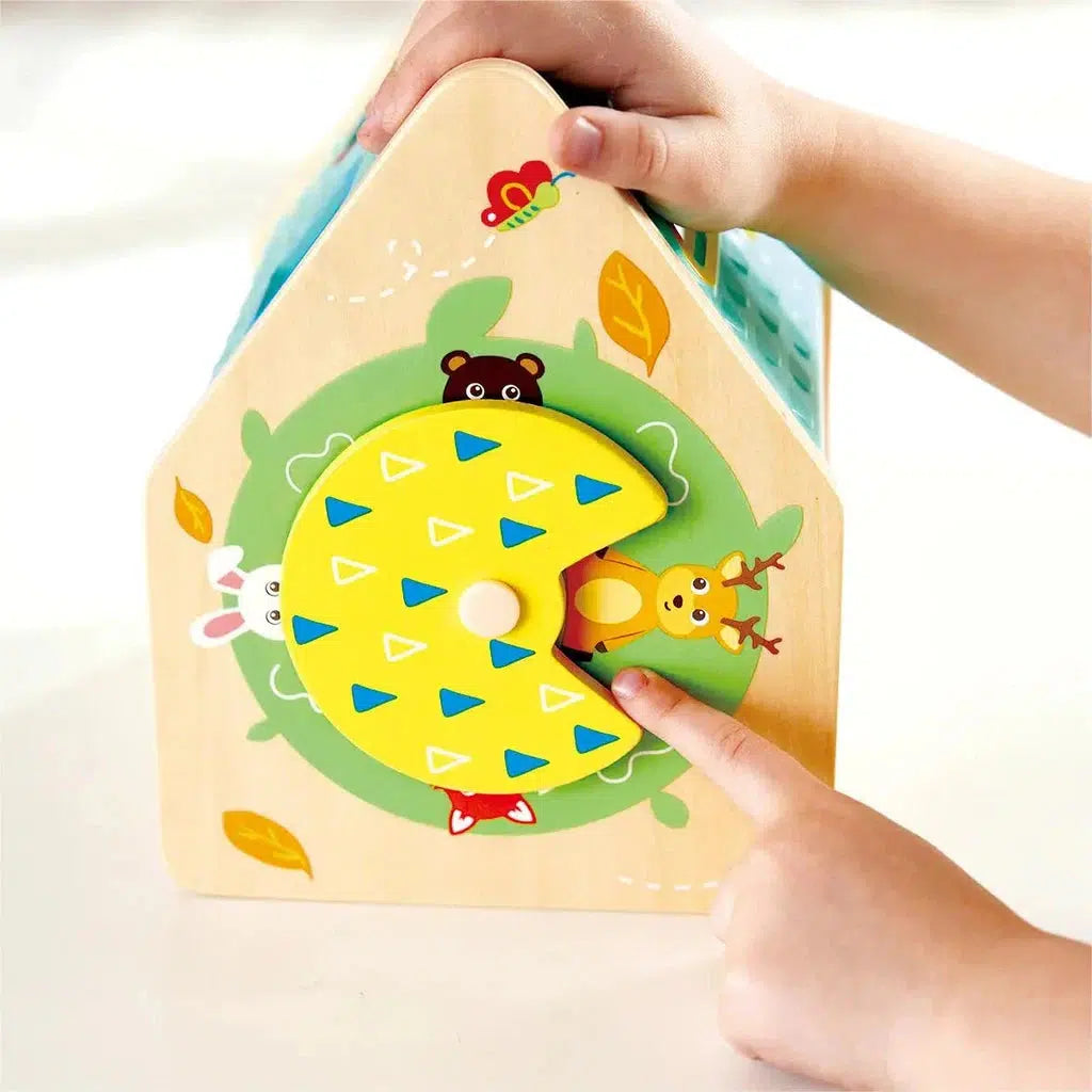 A child engages with a colorful wooden activity toy from Hape Toys featuring animals and a rotating wheel adorned with triangular patterns.