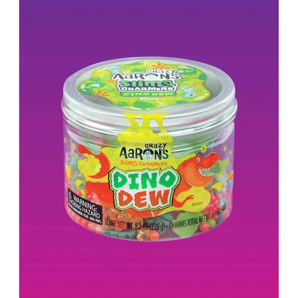 A container of Crazy Aaron's Dino Dew slime, labeled with "Slime with Charms" and "Collectible Tin," offers Jurassic fun. Featuring dinosaur-themed charms and vibrant graphics, it contains 8.2 oz (235 g) of bright green slime for a prehistoric playtime adventure.