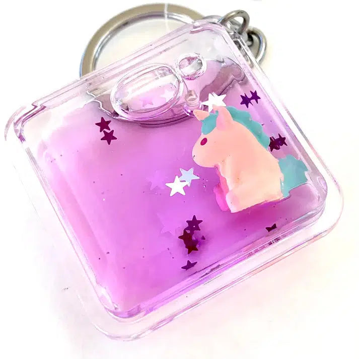 A clear keychain with a purple liquid interior features floating stars and a small, pastel-colored unicorn charm. This whimsical key ring adds a touch of magic to your everyday carry, perfect for those who adore silly animals and delightful accessories.