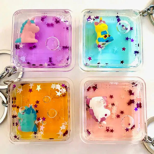 Four square keychains with colorful liquid, floating stars, and a charming floating unicorn charm in purple, blue, orange, and pink.