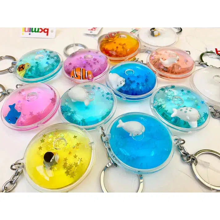 Colorful keychains with clear, round cases hold silly sea animals and floating star-shaped glitter. Attach this whimsical floating sea charm to your key ring for a touch of underwater fun!