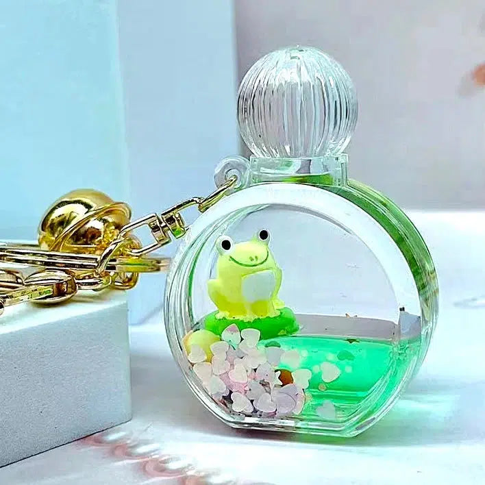 This delightful keychain features a tiny green frog figurine that seems to float like boba, surrounded by pink and white heart-shaped pieces, all encased in a clear round charm. It's attached to a gold clip for easy access, making it an adorable addition to any key charm collection.