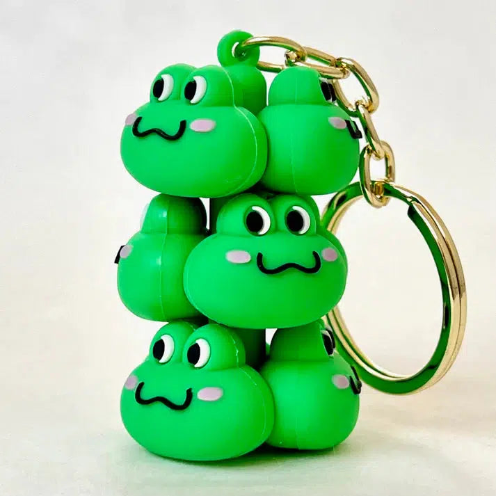 A delightful Frog Family Key Charm showcasing six stacked green frog-like figures with smiling faces and pink cheeks. This silly animals keychain adds a touch of playful charm against a plain background.