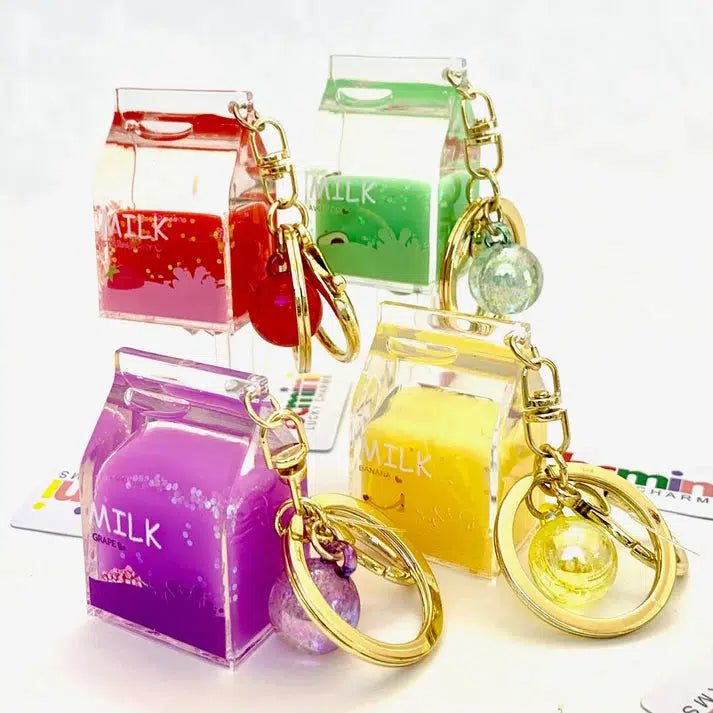 Colorful milk carton-shaped keychains in red, green, yellow, and purple arranged on a white surface, each adorned with a matching spherical charm and a whimsical Fruit Milk Key Charm on the key ring.