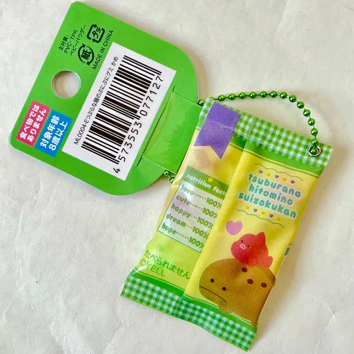 A whimsical keychain mimics a snack bag with vibrant Japanese text, featuring an assorted design and attached to a green chain. Perfect for adding a touch of fun to your keys, this Turtle Gummy Key Charm is a playful accessory in the Silly Animals series.