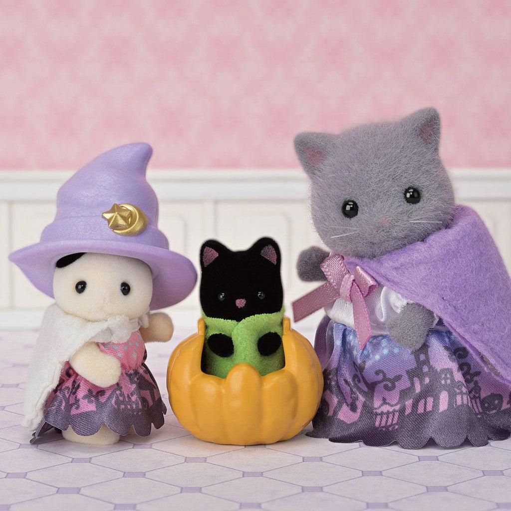 Three Calico Critters dressed in witch costumes stand together; one is in a pumpkin. The background is pink with a hexagonal floor.