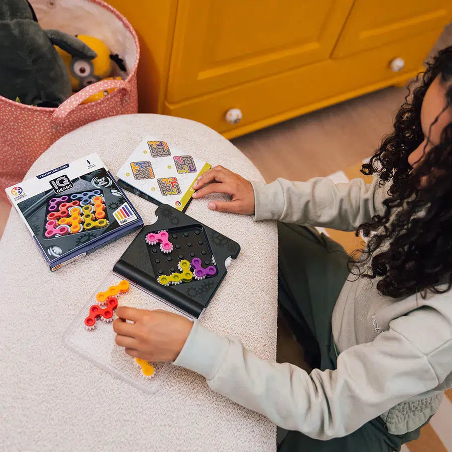 A child is deeply engaged with a colorful IQ game on the table, surrounded by game pieces and instruction cards, exploring brain games that offer 120 challenges.