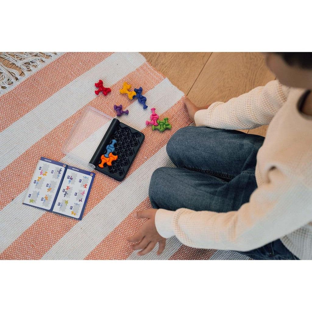 A person sitting on a striped rug next to an IQ-Waves puzzle game with colorful pieces and an educational instruction booklet.