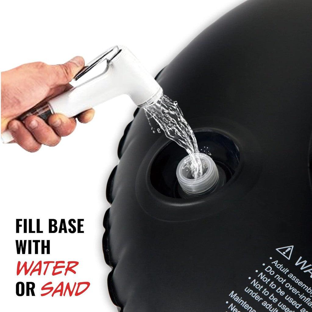 A hand fills a black inflatable base with water using a white hose, setting up the Kickboxing Punch Bag. Text reads: "FILL BASE WITH WATER OR SAND." Perfect for your Sports &amp; Outdoors adventures.