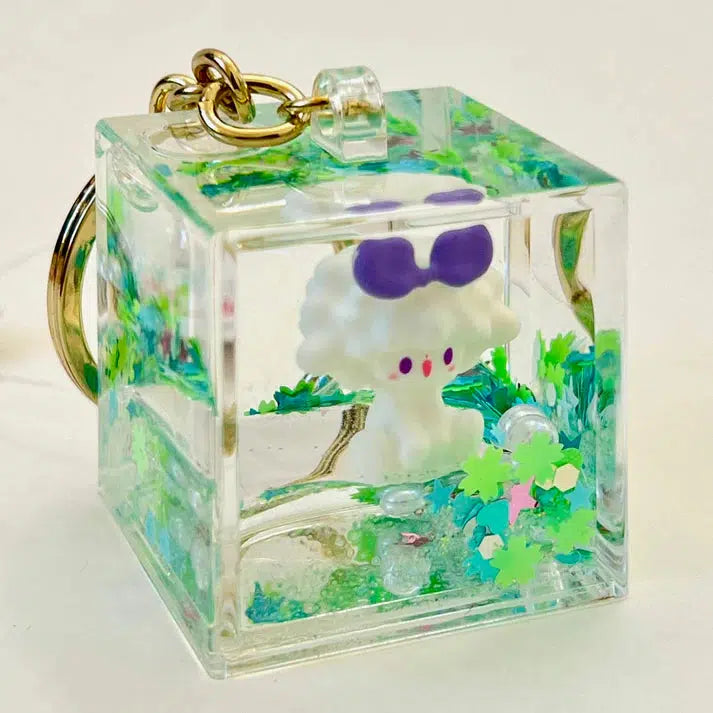 This charming cube-shaped key charm encases a cute, white figurine with purple ears, enveloped in green and colorful confetti-like decorations. Part of an assortment of silly animals, it's perfect for adding a touch of whimsy to your keys.