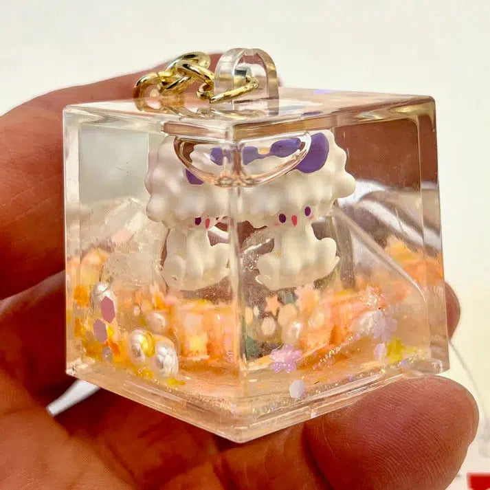 The Lamb Floaty Key Charm is a decorative keychain featuring a cute character encased in a transparent cube with colorful embellishments at the base, part of our Silly Animals series.