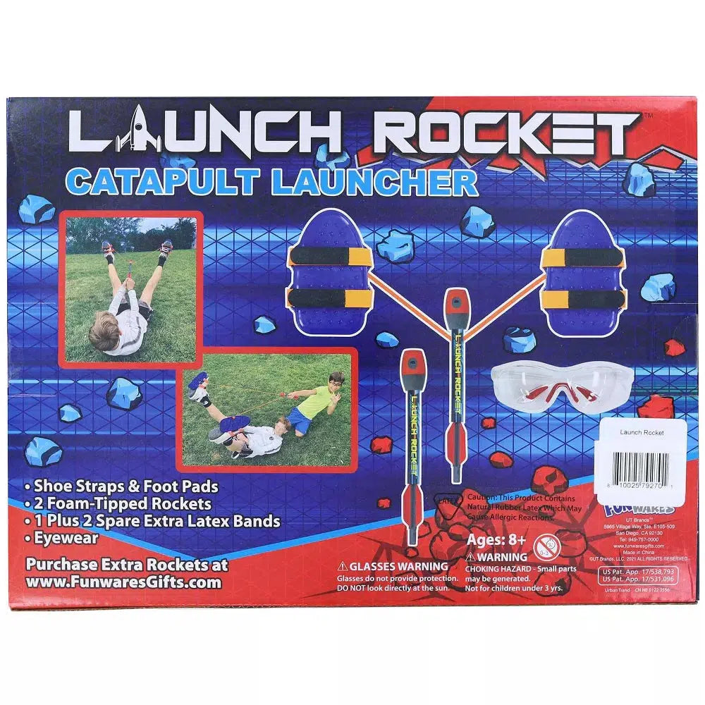 The UT Brands Rocket Catapult Launcher box displays vibrant images of its use, showcasing included items like shoe straps, foam-tipped rockets, latex bands, and eyewear. Perfect for hitting your target every time. Recommended for ages 8 and up.