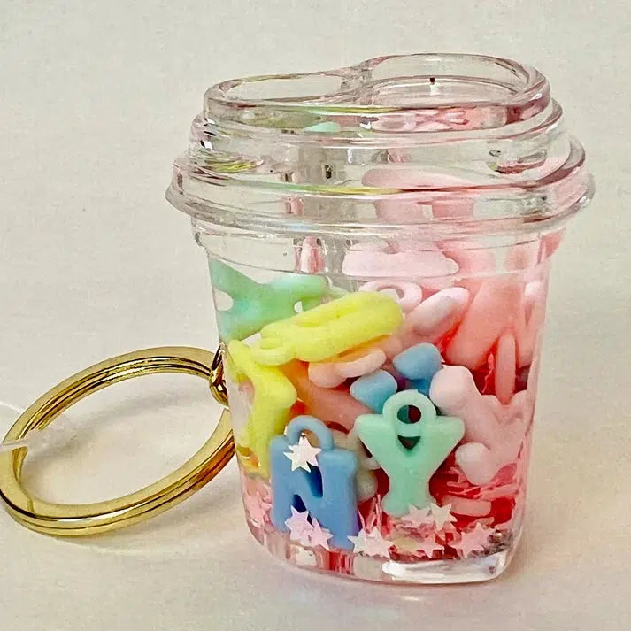 A clear plastic container with a keyring, featuring colorful pastel letter beads, star-shaped charms, and a floaty key charm in assorted designs.