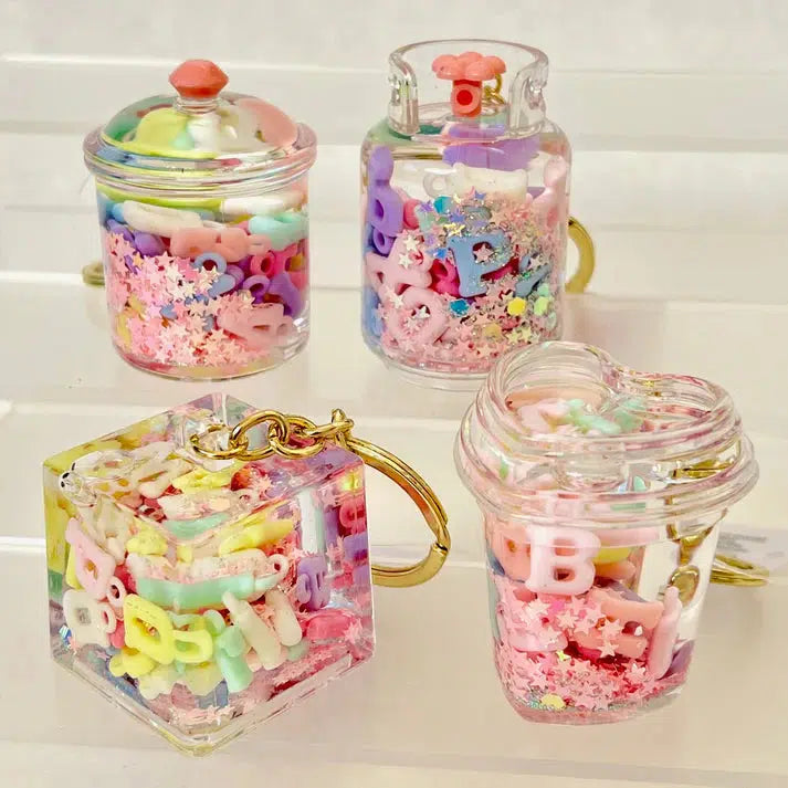 Four transparent keychain containers filled with colorful alphabet beads and decorative shapes, featuring assorted designs and silly animal charms.