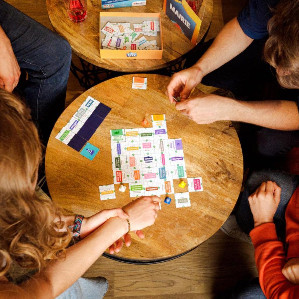 People sitting around a circular wooden table, engaged in a cooperative party game with cards and pieces, immerse themselves in the strategic world of Link City Board Game.