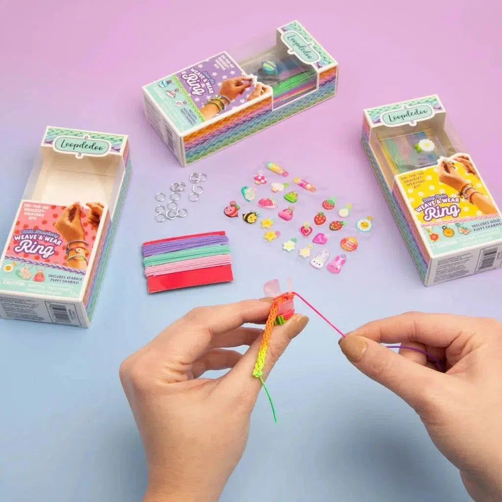 Hands crafting with colorful strings and rings, surrounded by craft kits and charm decorations on a pastel background.