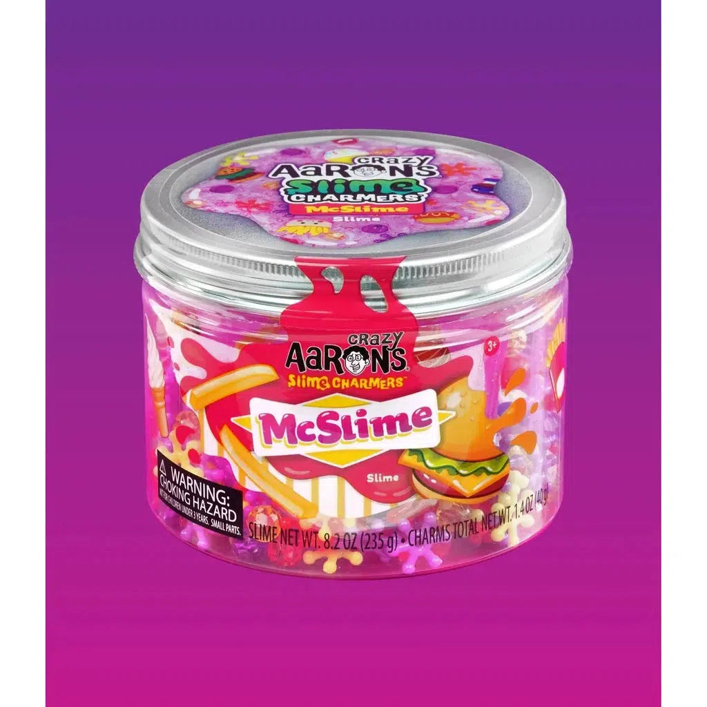 A clear plastic container labeled "Crazy Aaron's Slime Charmers, McSlime" is filled with watermelon-scented purple slime and small slime charms, set against a vibrant purple background.