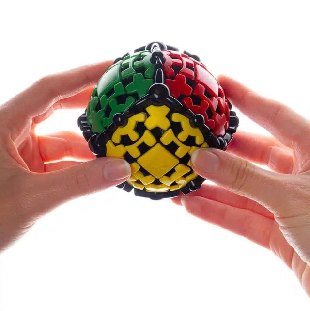 Hands gently cradle a Gear Ball, its interlocking pieces in vibrant red, green, and yellow forming a perfect spherical twisty puzzle against a white background. Inspired by the ingenious designs of Uwe Meffert, it invites curiosity and challenge.