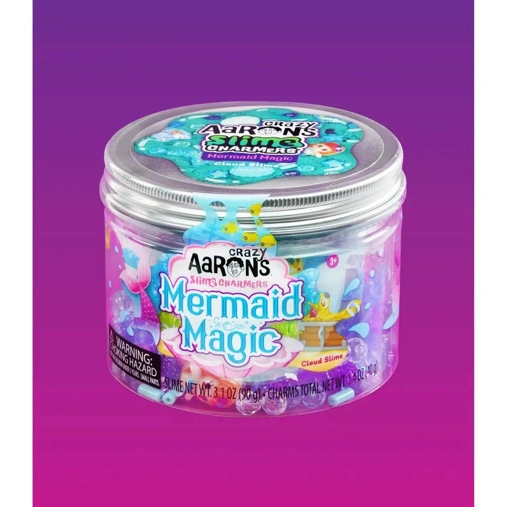 A container of Crazy Aaron's Slime Charmers Mermaid Magic in teal cloud slime with charms, featuring 3.1 oz (90.9 g) of fun. The package is colorful with ocean-themed graphics.