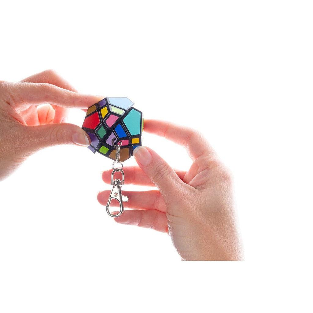 Hands holding a colorful dodecahedron puzzle keychain against a white background.