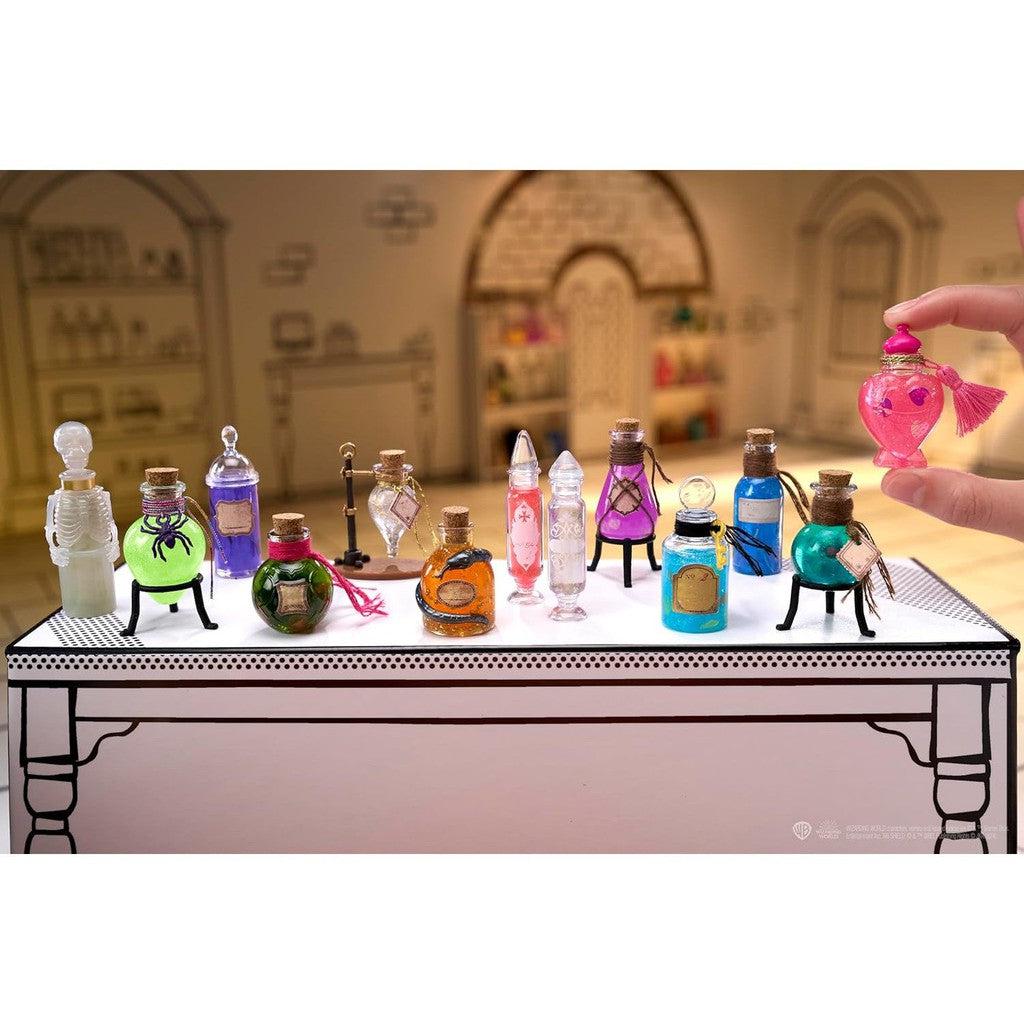 A collection of colorful potion bottles, reminiscent of Harry Potter's world, is displayed on a table. A hand holds a pink heart-shaped bottle with a tassel. These enchanting mini collectibles capture the charm of replica potions for every aspiring wizard's shelf.