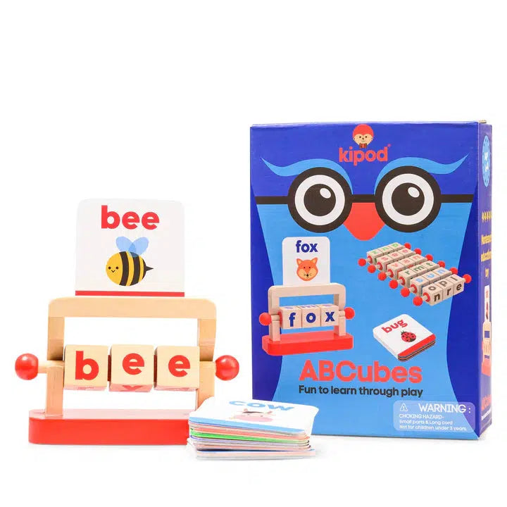 A wooden educational toy set containing block letters and illustrated cards for children spelling and word formation. The box is labeled "kipod ABCubes" and includes a picture of the Montessori Reading Blocks toy alongside sample words.