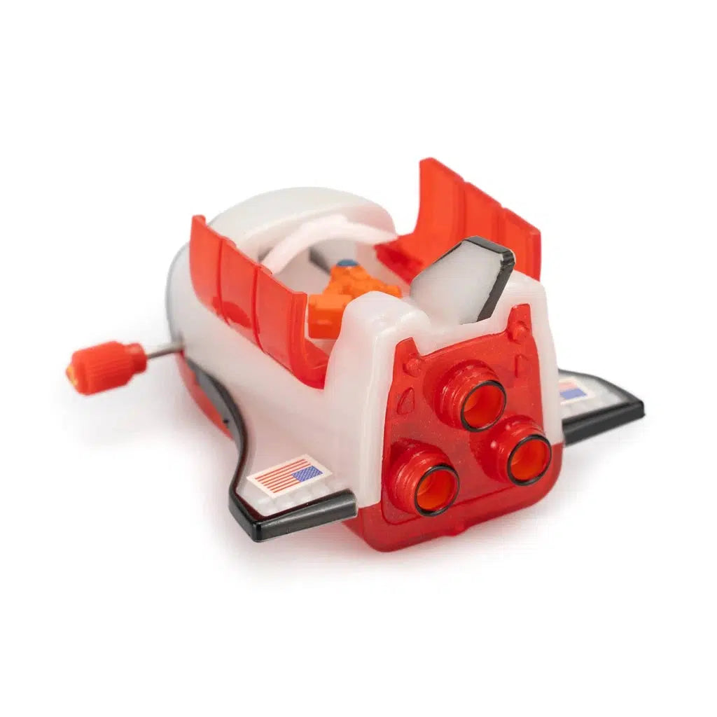 Wind-up toy space shuttle with red accents, three rear engines, and small American flags on the wings, ready for an imaginary spacewalk adventure on a white background.