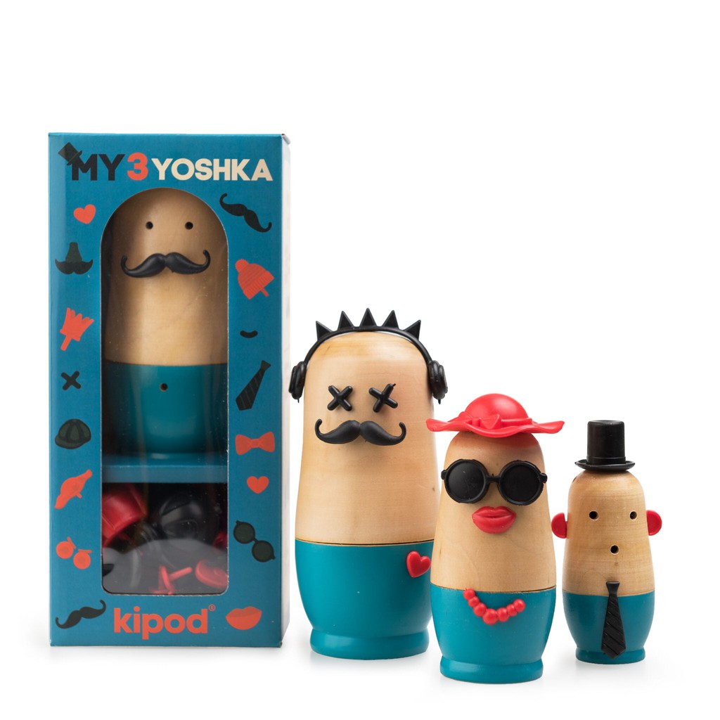 Three wooden nesting dolls with various features such as interchangeable glasses and hats, standing next to a box labeled "My 3 Yoshka" by Kipod, 