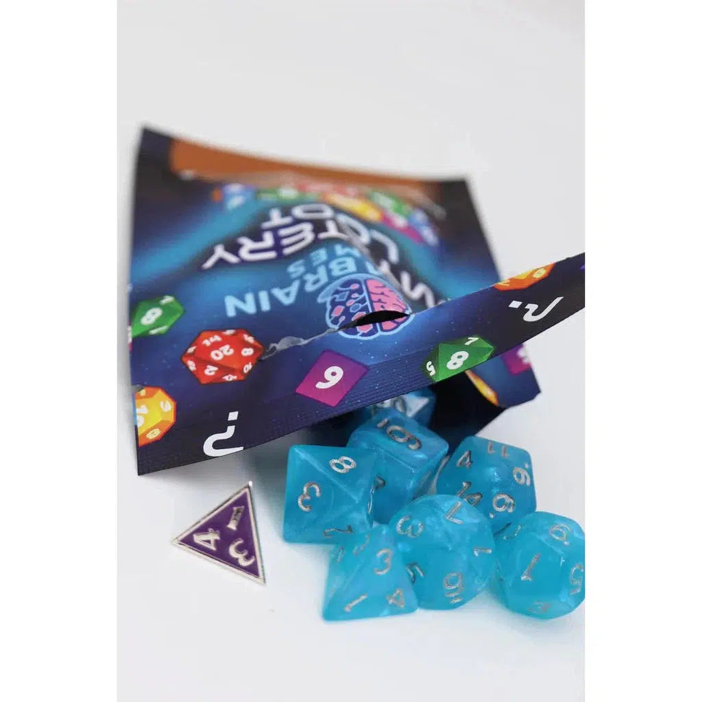 A mystery set featuring a pack of multicolored brain candy and blue plastic RPG dice is displayed, with one triangle-shaped pin. Perfect for Foam Brain fans looking to add some intrigue to their collection.