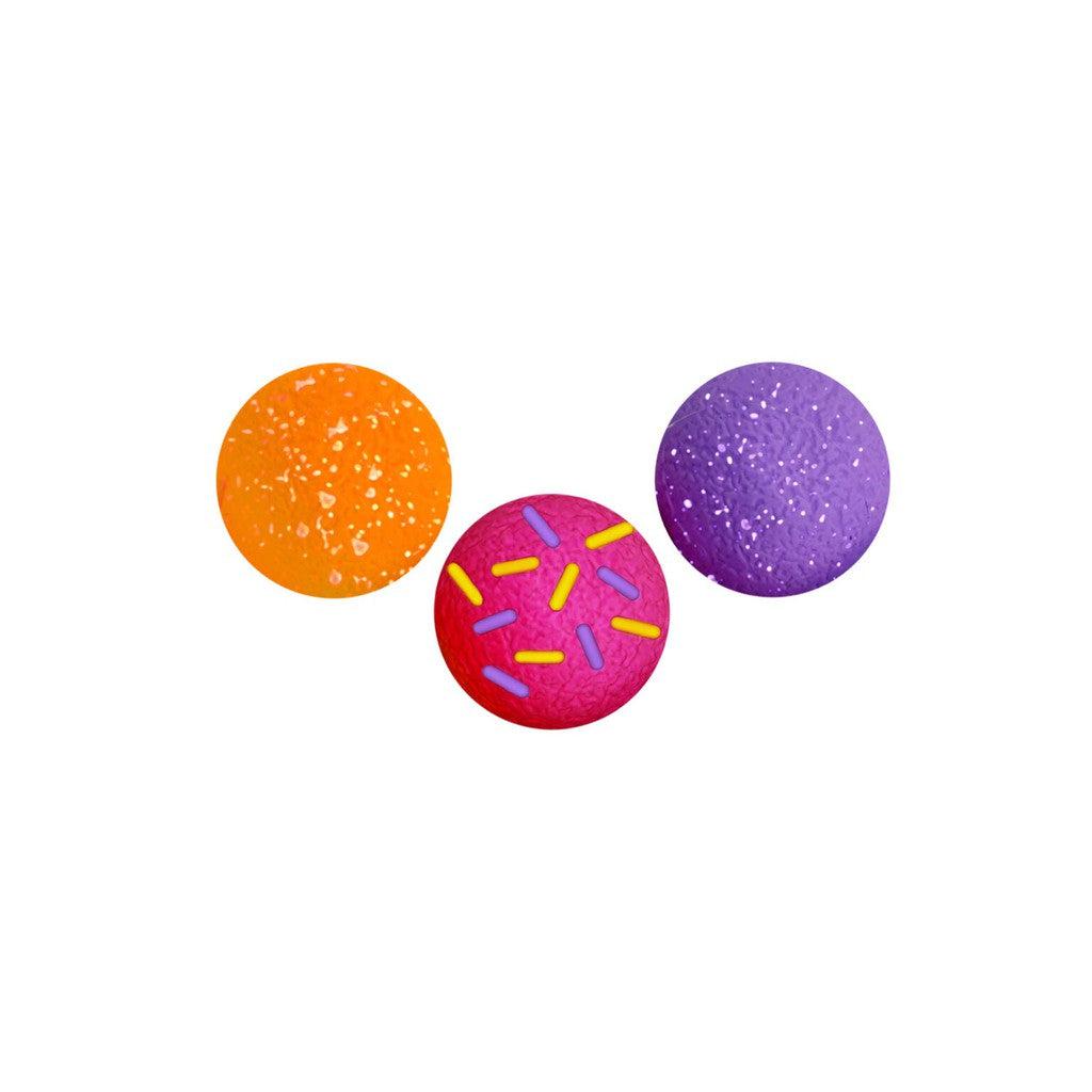 Three vibrant textured balls—one orange, one purple, and one red with yellow and purple sprinkles—sit in a triangular formation on a white background, offering a delightful sensory experience reminiscent of NeeDoh Dohnut Holes.