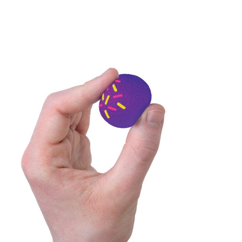 A hand is holding a small, purple ball with pink and yellow sprinkles on its surface, resembling NeeDoh Dohnut Holes. It's a delightful sensory experience that adds to the playful charm of this unique object.