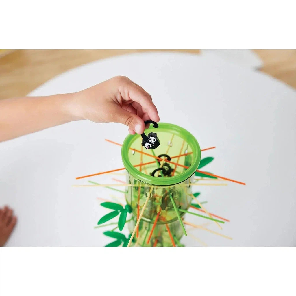 Child's hand placing a panda figure into a green tumbler filled with colorful sticks, resembling a game.