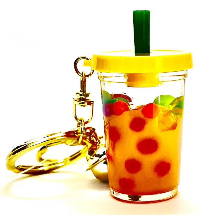 A whimsical key charm shaped like a bubble tea cup, featuring a pastel boba floaty design with a yellow lid, green straw, and orange liquid filled with red bubbles inside.