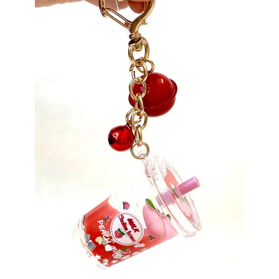 Key charm featuring a small pink drink cup with a straw, decorated with fruit and stars, and two attached red bells, all part of assorted designs.