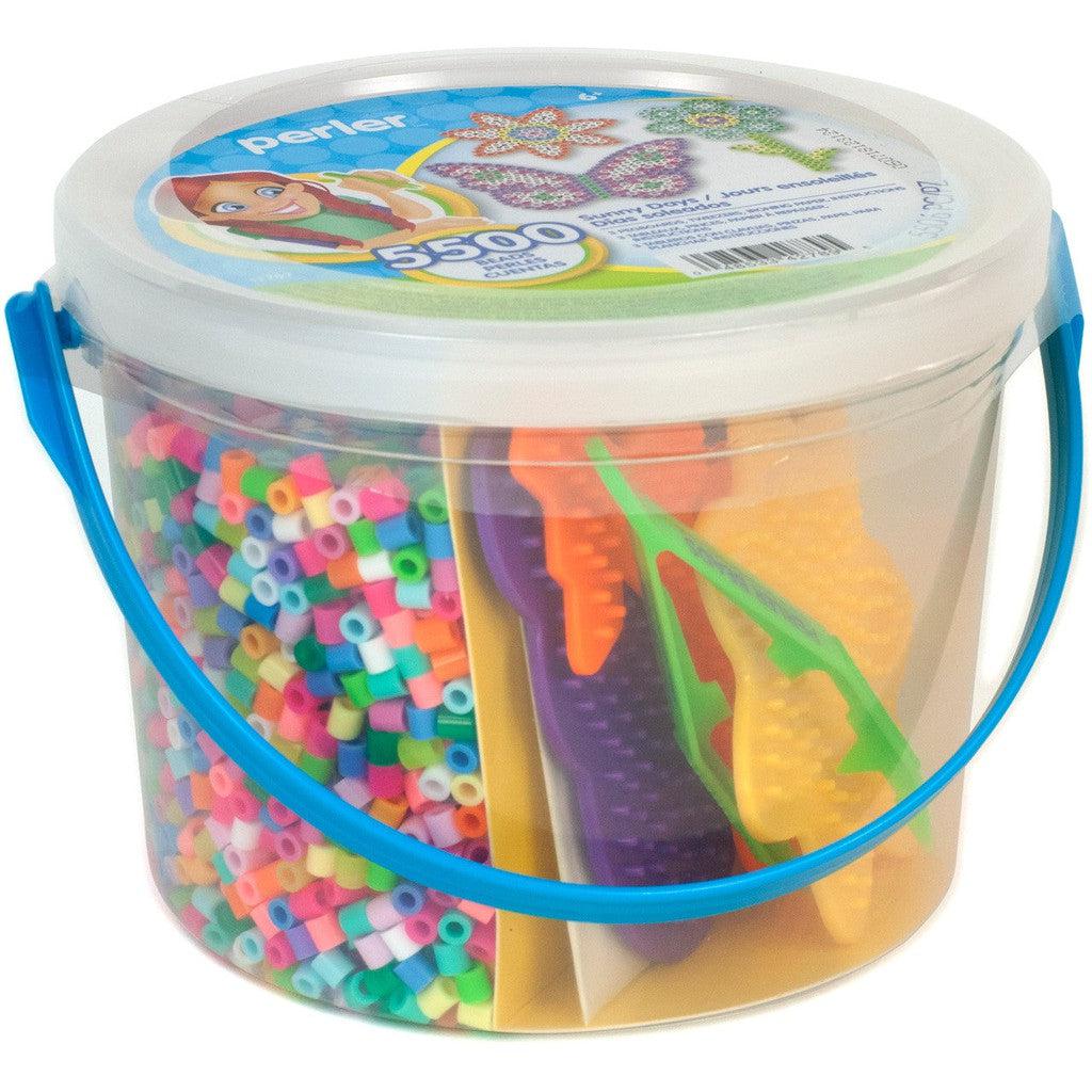 A cylindrical plastic container with a blue handle holds multicolored Perler beads and various shaped pegboards. Labeled as an Activity Bucket, it contains 5500 beads.